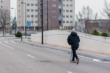 Hombre joven que viste de negro montando en patinete plegable por una carretera de la ciudad vacía.