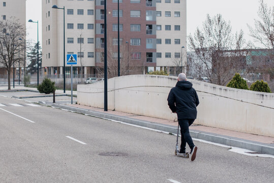 Hombre joven que viste de negro montando en patinete plegable por una carretera de la ciudad vac&iacute;a.