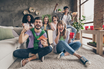 Obraz premium Portrait of nice amazed cheerful friends sitting on carpet having fun eating snack watching cinema laughing in house loft brick style interior indoors