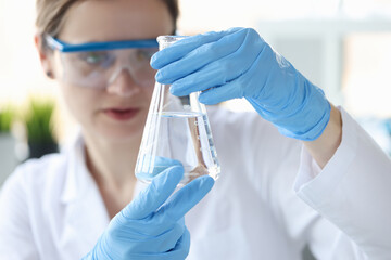 Woman scientist holding flask with transparent liquid in her hands closeup