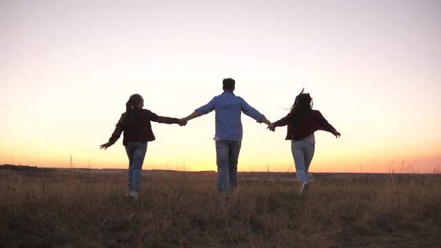 Free happy family runs across field holding hands. Dad, mom and daughter are playing cheerfully, running with raised hands, teamwork. Family travels on vacation. Father, mother, child