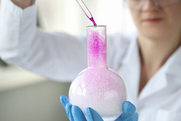 Woman scientist dripping liquid from pipette into chemical flask closeup