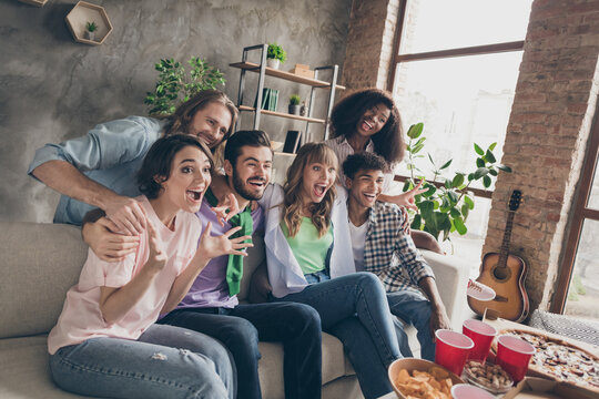 Portrait of attractive overjoyed cheerful friends gathering sitting on sofa having fun watching film in house brick loft style indoors