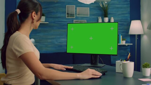 Freelancer looking for marketing information on internet using personal computer with mock up green screen chroma key. Business woman working with isolated pc at office desk in living room
