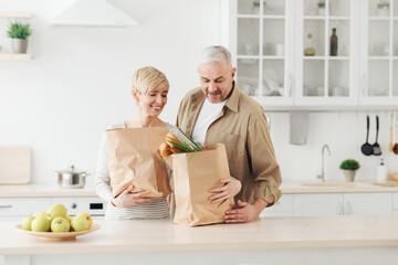 Ordering food online. Senior couple arriving from supermarket with grocery bag and unpacking in kitchen