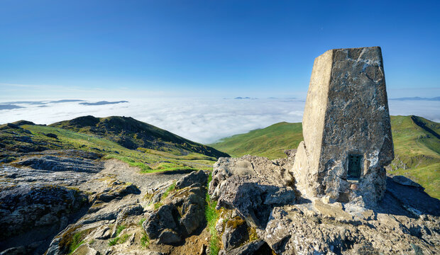 The trig point marker on the mountain summit of Ben Lawers looking out over the mountain sumit of Beinn Ghlas and Meall nan Tarmachan with a cloud Inversion covering Loch Tay in the Scottish Highlands