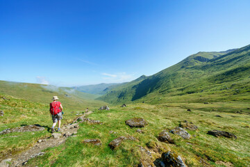 Fototapeta na wymiar A female hiker walking along a mountain path to the summit of Meall Corranaich with the glen of Allt a Chobhair below and the summit of Carn Gorm in the distance. Scottish Highlands, UK landscape.