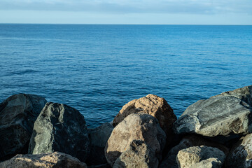 Fototapeta na wymiar Steinküste Gran Canaria bei Sonnenaufgang und ruhiger See mit leichtem Wellengang