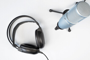 Studio microphone on a stand and black headphones on a light background, top view. Professional equipment for online broadcasting. Podcast concept.