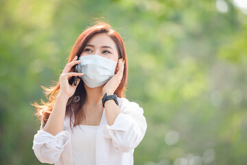 Young asian women Wearing a mask to prevent COVID-19 is using a smartphone on the street on a sunny hot summer day in the park.