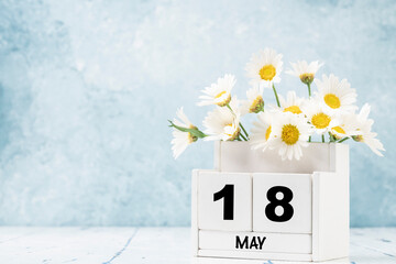cube calendar for May decorated with daisy flowers over blue with copy space