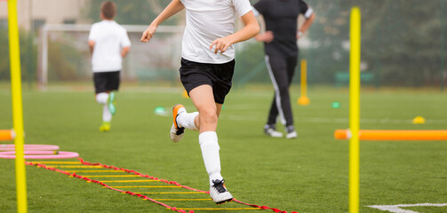 Young boy in soccer shoes cleats running through training ladder. Coach in the background. Football...