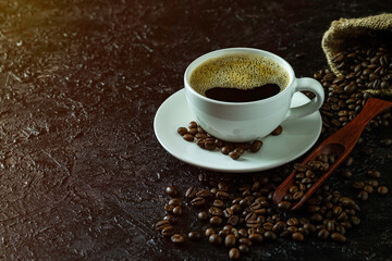 Hot black coffee for morning beverage menu in white ceramic cup with coffee beans roasted in burlap sack bag on dark grunge rustic table background. Flat lay with copy space.