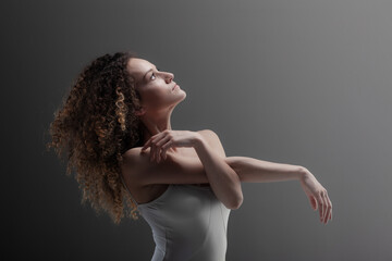 Naklejka premium Girl with curly hair making ballet poses. Ballerina in white dress
