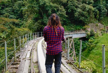 Naklejka premium Man from behind with dreadlocks and square shirt standing on the train tracks on a bridge