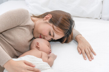 Obraz na płótnie Canvas Close up beautiful young asian mother kissing her newborn one month baby sleep in bed. Healthcare and medical love asia woman lifestyle mother's day concept.