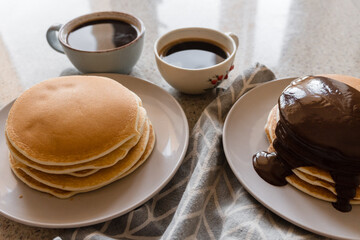 Cups of coffee and plates with pancakes drizzed with chocolate