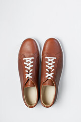 Leather brown men's sneakers with white laces and rubber soles on gray background. Flat lay top view. Men's sports casual shoes. Fashionable sneakers. Male fashion, hipster footwear Minimal background