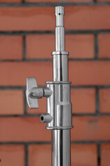 metal light stand with fastening mechanism above a red brick wall background