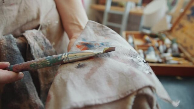 Close up shot of hands of unrecognizable female artist cleaning paintbrush with cloth after painting a picture