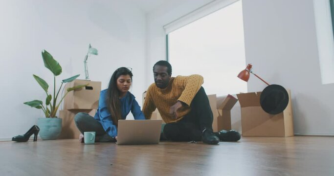 Multi-ethnic couple in their new apartment surrounded by cardboard boxes are shopping online
