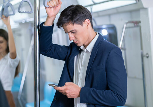Businessman gets on a train to work in the morning and stands by typing on a smartphone and reading online messages on the underground train.