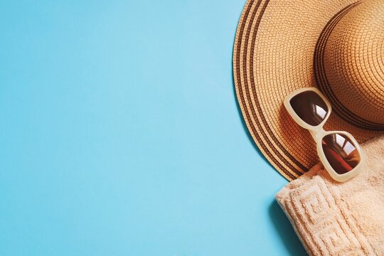 Summer travel beach essentials top view photography. Yellow straw hat, brown sunglasses and beige towel on a blue background. Mockup, flat lay image, free space for text