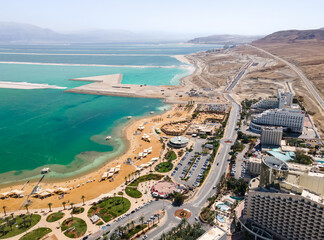 Obraz na płótnie Canvas Aerial view from a drone of the beach on the Ein Bokek embankment on the coast of the Dead Sea, the sea itself and the mountains of Jordan visible in the distance, in Israel