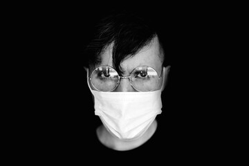 Black and white photo of a portrait of a young man with glasses. Holds her bangs with her hand. Close your forehead. On a black background. He holds his glasses. A serious face. Businessman.