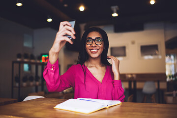 Cheerful African American woman taking selfie on smartphone