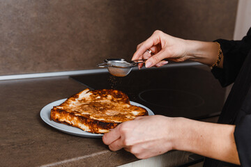 woman sprinkles cocoa powder with hot cake at home in kitchen