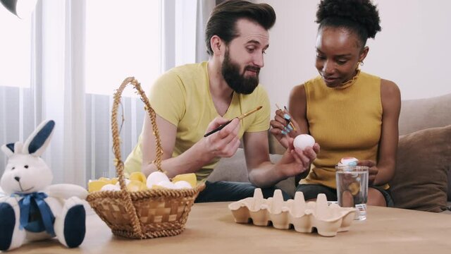Black woman and European man painting Easter eggs together