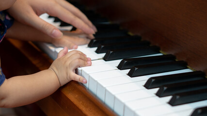 Fototapeta premium Side view of Baby Girl's Hands playing with Piano Keys with an adult