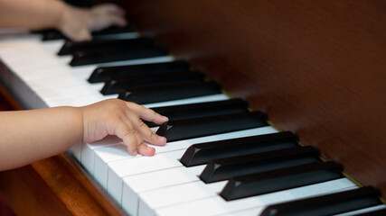 Fototapeta premium Side view of Baby Girl's Hands playing with Piano Keys with an adult