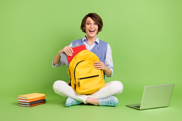 Portrait of attractive cheerful amazed girl sitting lotus position packing bag highschool isolated...