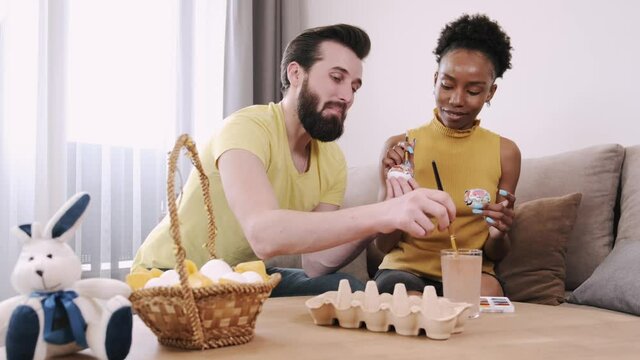 Black woman and European man painting Easter eggs together