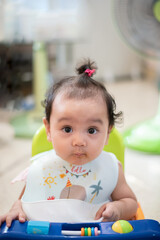 Fototapeta premium Portrait of happy Asian baby sitting on the dining table, looking at the camera