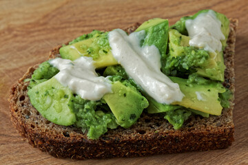 Close-up view of sandwich with avocado spread on bread slices with tahini and yoghurt dressing.