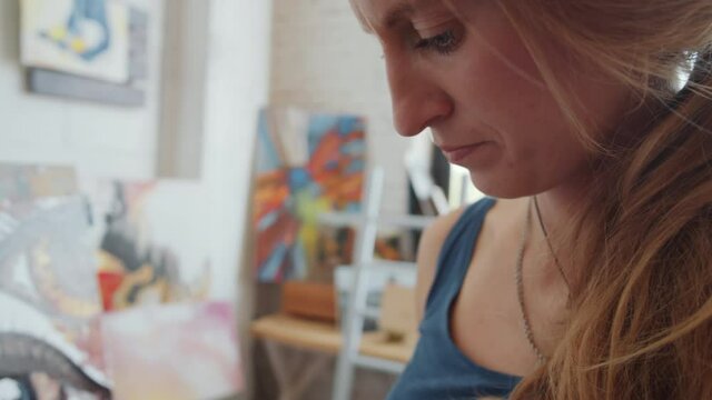 Close up shot of young female artist painting contemporary art picture with oil paints in studio
