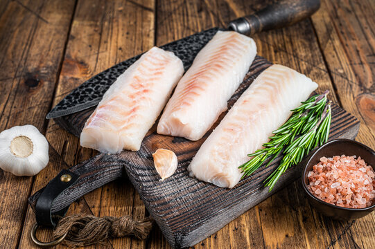 Fresh Raw cod loin fillet steaks on wooden board with butcher knife. wooden background. Top view
