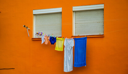 Ropa tendida entre dos ventanas cerradas por persianas en una fachada de intenso color naranja