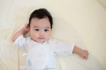 Fototapeta premium Top view of a cute little Asian baby girl lying on the bed, looking at camera