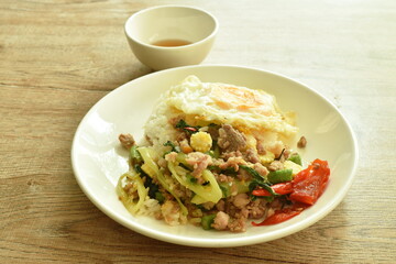 spicy stir fried chop pork with vegetable and basil leaf on rice couple egg in plate dipping chili fish sauce cup