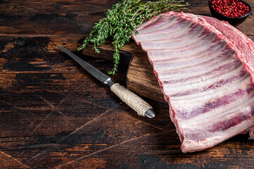 Mutton lamb ribs rack on wooden cutting board. Dark wooden background. Top view. Copy space