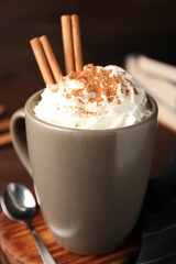 Cup of hot drink with aromatic cinnamon and whipped cream on wooden table, closeup