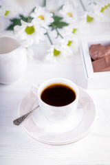 White cup of black coffee, chocolate candies and chrysanthemums flowers