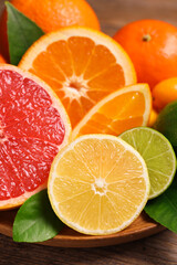 Fresh juicy citrus fruits with green leaves on wooden plate, closeup