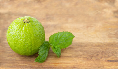 One green whole lime with mint leaves on a wooden background