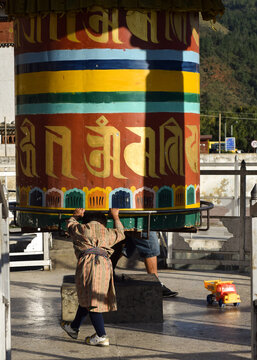A child wearing traditional bhutanese clothes spinning a big prayer wheel in downtown Paro, Bhutan.