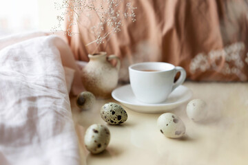 Easter cozy still life composition with qual eggs, cup of tea and beige cloth. Morning teatime